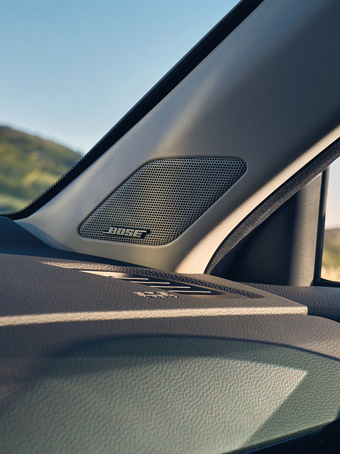  Et nærbilde av en Bose-høyttaler integrert i den innvendig A-stolpen i en bil, plassert nær dashbordet og frontruten.