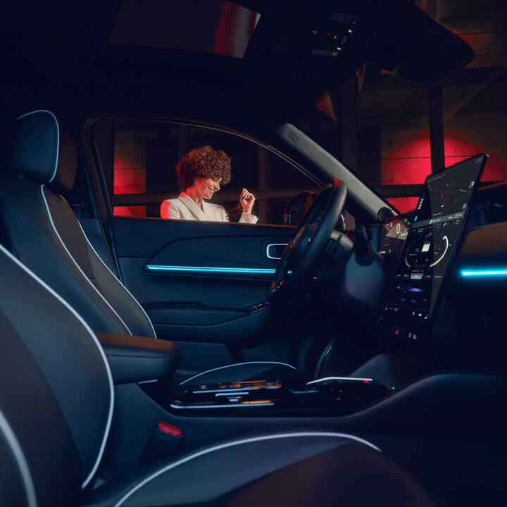 Opplyst interiør på Honda e:Ny1 om kvelden med modell utenfor vinduet.