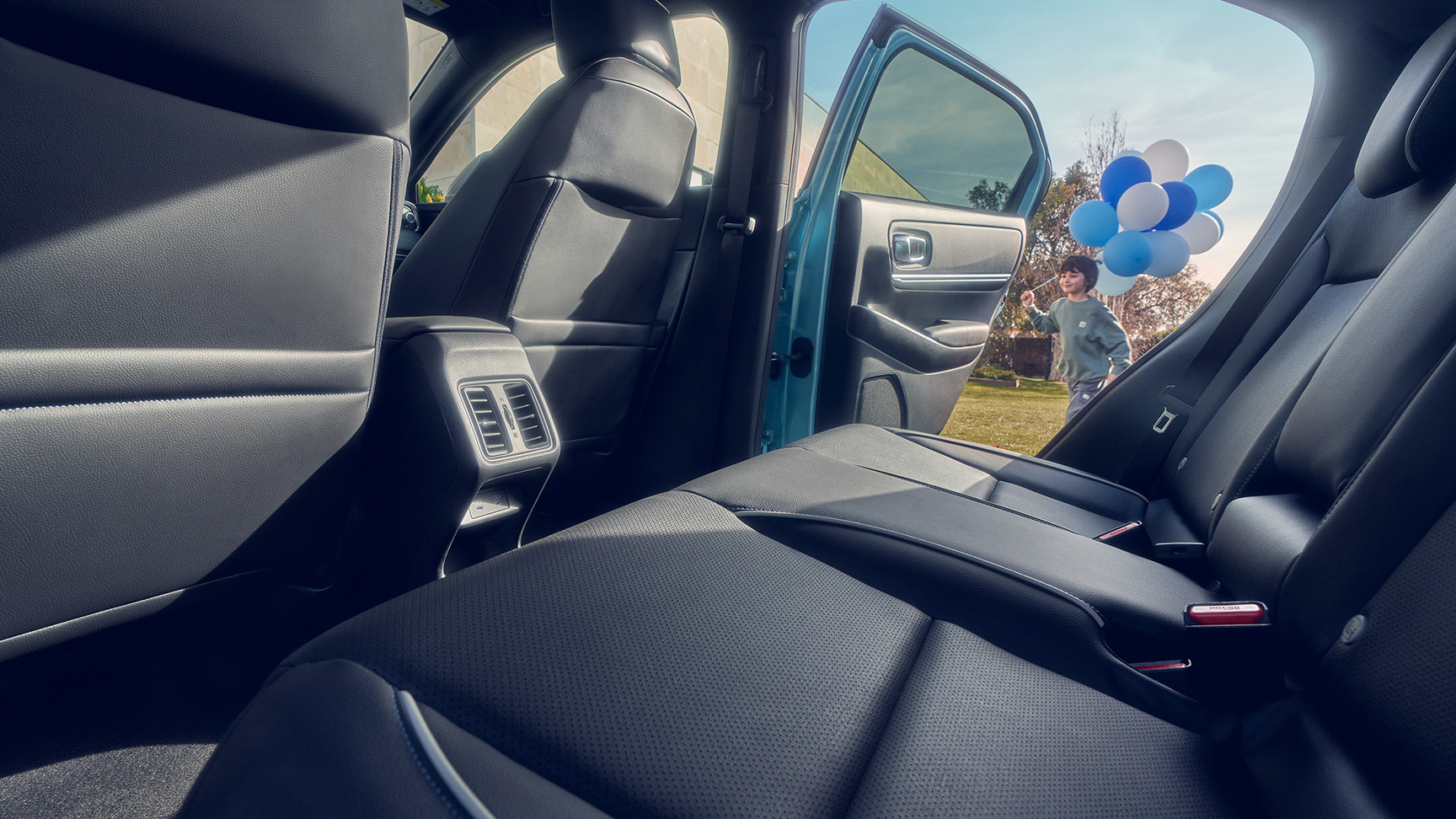 Nærbilde av baksetet i Honda e:Ny1 med barn som holder ballonger og går forbi åpen dør.