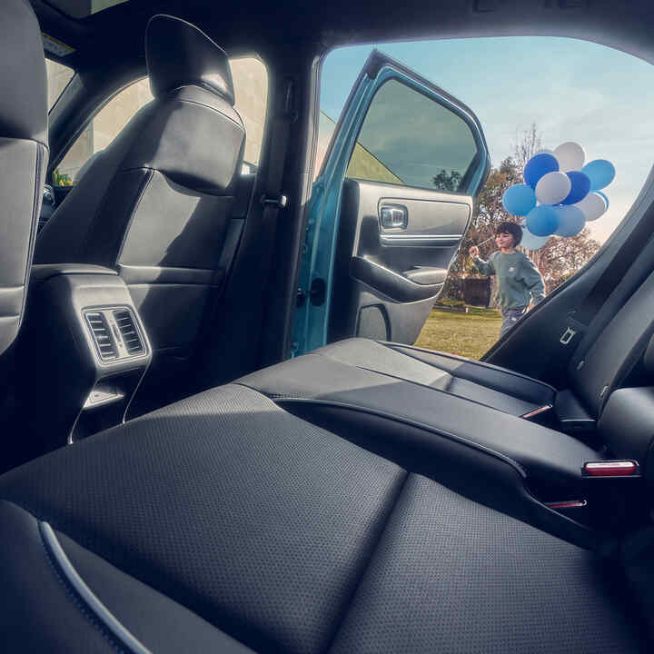 Nærbilde av baksetet i Honda e:Ny1 med barn som holder ballonger og går forbi åpen dør.