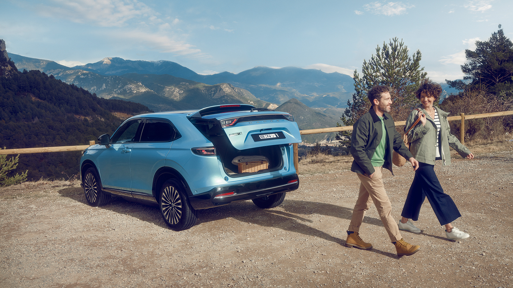 Honda e:Ny1 sett skrått bakfra i fjellområde med et par som går av sted.