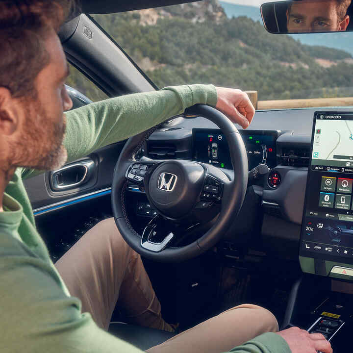 Mann som kjører i Honda e:Ny1 ved hjelp av navigasjon på det digitale førerdisplayet.