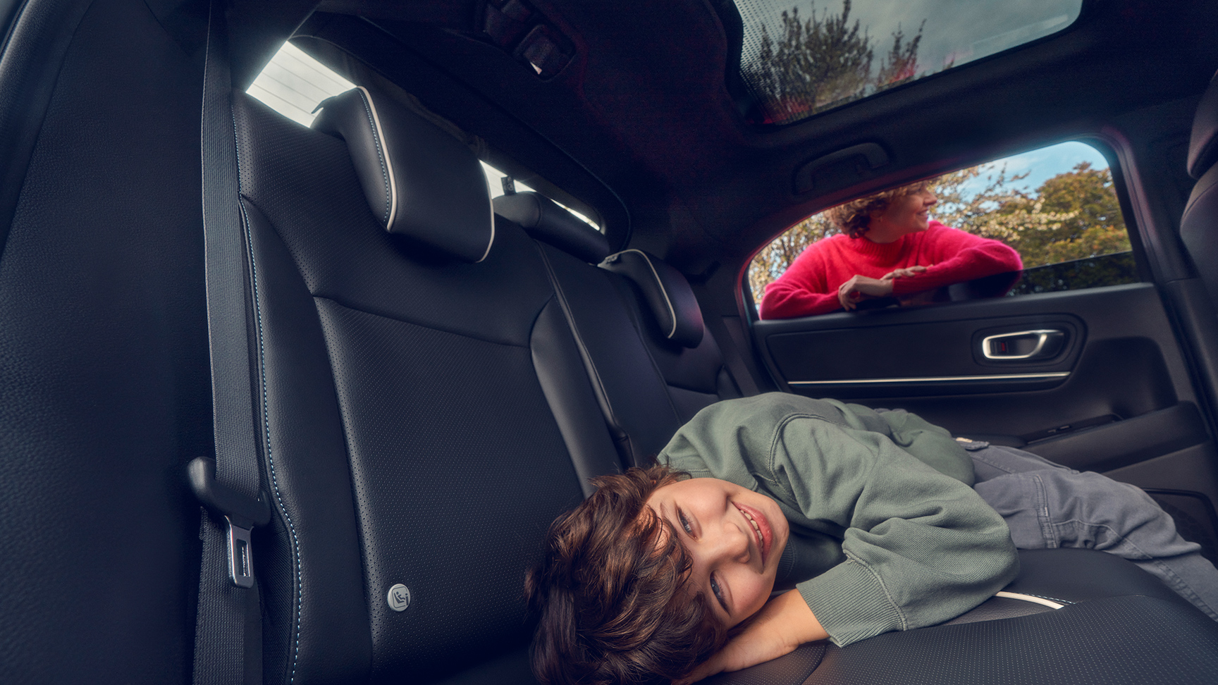 Barn som ligger på baksetet med mor som står i vinduet på Honda e:Ny1.