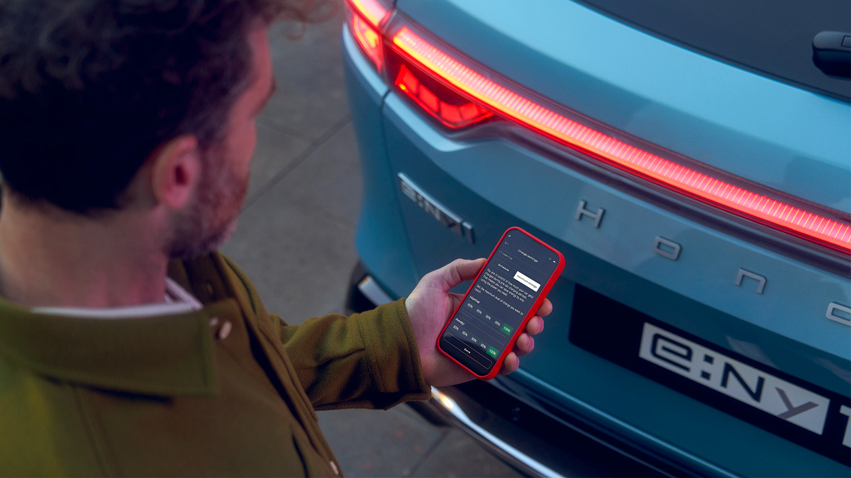 Mann ser på My Honda+-appen ved siden av Honda e:Ny1