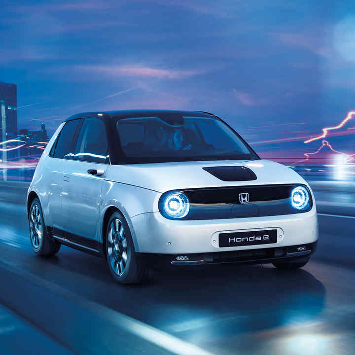 Honda e som kjører gjennom et elektrisk bybilde, sett skrått forfra.