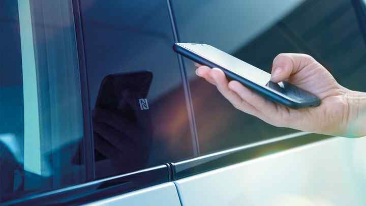 My Honda+-app – nærbilde av person som bruker telefonen utenfor bilen