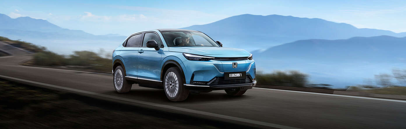 En blå Honda e:Ny1 kjører på en landevei med fjell i bakgrunnen.