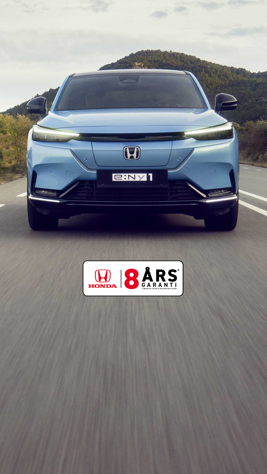 Honda e:Ny1 i Aqua Topaz Metallic kjører på en svingete vei med grønne åser i bakgrunnen.